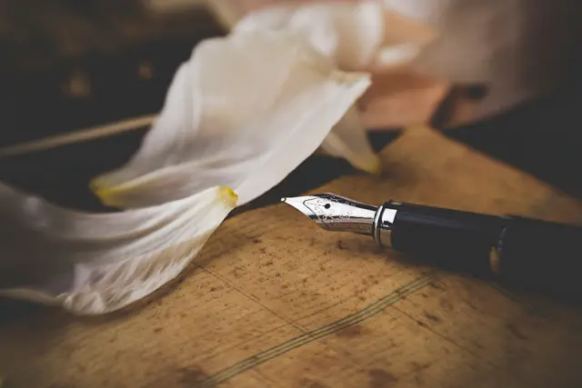 A fountain pen resting on handwritten paper beside white lily petals